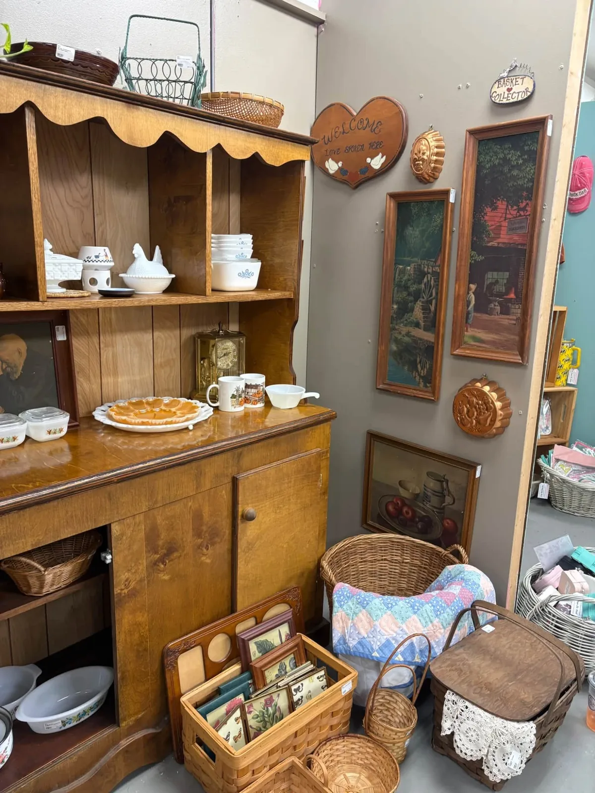 A corner of the booth: a heart shaped Welcome sign, copper molds, framed paintings and a woven picnic basket